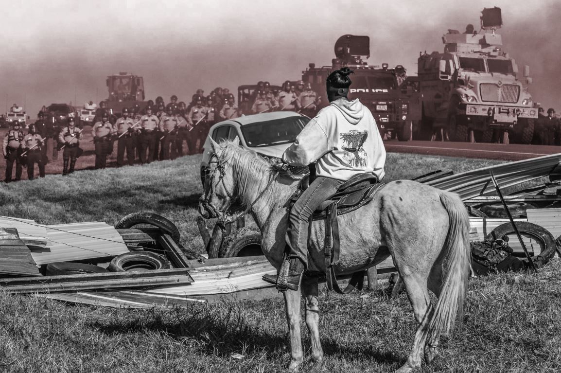 Native American on horseback facing line of police and trucks.