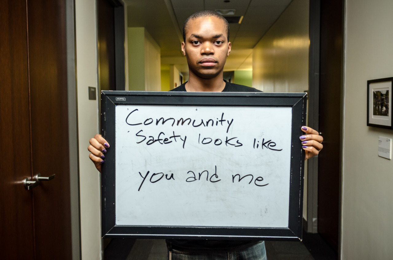 Man holding sign that says, "Community safety looks like you and me"